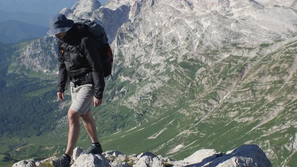 A tourist with a backpack on his back is walking through the mountains behind him is a mountain peak alt