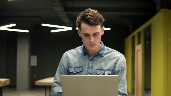 Young Attractive Guy in Denim Shirt with Laptop in His Hands is Walking Somewhere in Well Lit alt