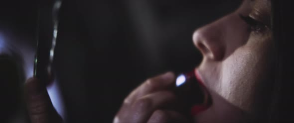 Young woman looking in the mirror applying lipstick alt