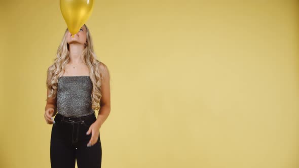 Sexy Model Throwing and Catching a Yellow Ballon Against Yellow Background alt
