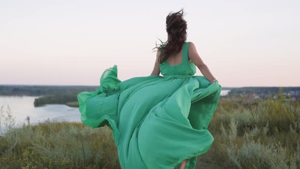 a Young Woman in a Green Long Dress Runs on the Background of a Beautiful Landscape alt
