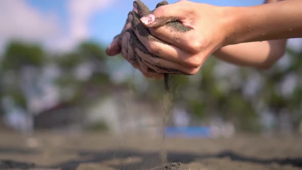 close-up hand grabs a handful of dry sand and lets it fall between his fingers alt