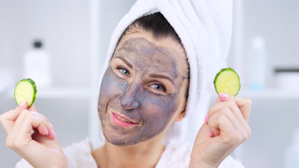 Girl Using Natural Cosmetic Face Mask and Fresh Cucumbers alt