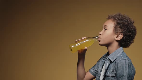 Little Boy Drinking Juice From Bottle on a Yellow Background Side View