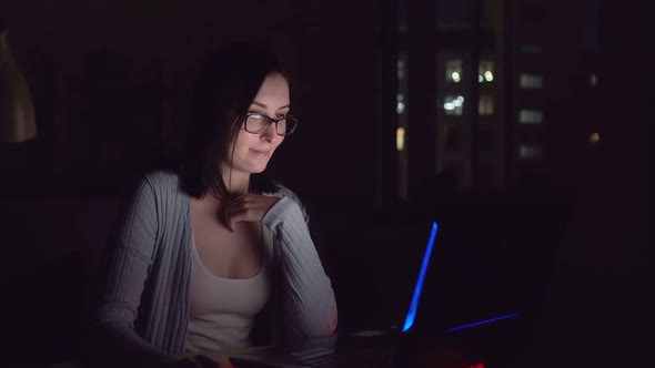 Cute Young Woman Smiling in the Dark Looking at Laptop Screen at Home alt