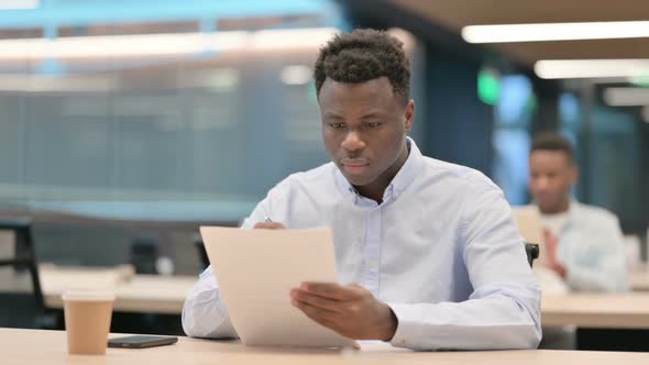 African Businessman Celebrating Success While Reading Documents alt