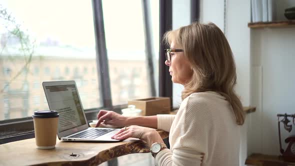 Woman Journalist Sit in Cafe with Laptop and Type Write an Article Text alt