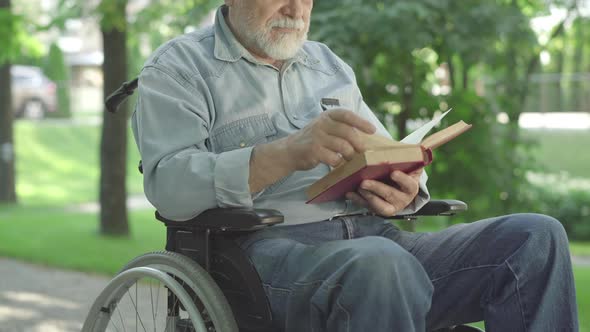 Unrecognizable Paralyzed Senior Man Turning Book Page and Reading Out Loud. Old Grey-haired Male alt