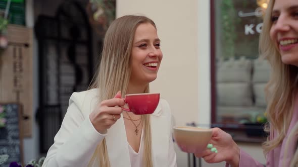 Young adult women talking smile laugh and drink coffee at street bar outdoors. Two female persons alt