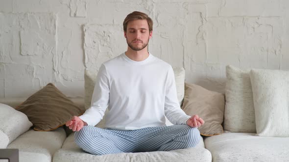 Wellness Young Man Sits on a Sofa in the Living Room and Meditates a Calm Mood Relaxing in a White alt