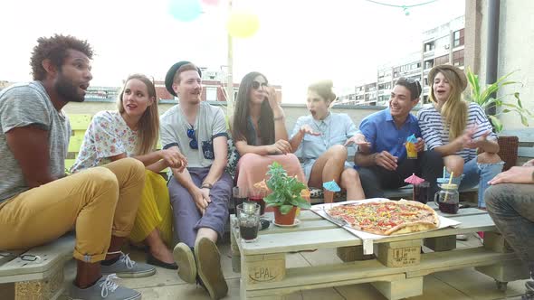 Attractive young people sitting around the table on the rooftop terrace alt