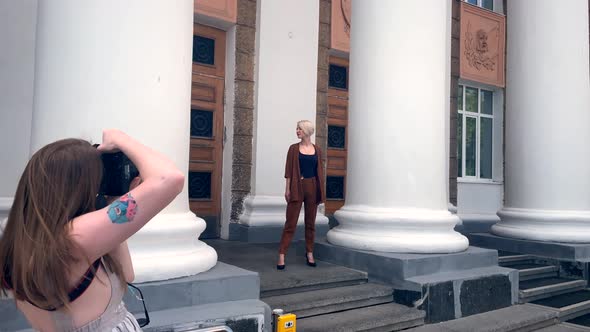 A Young Blonde Poses for a Photographer Against the Background of White Columns
