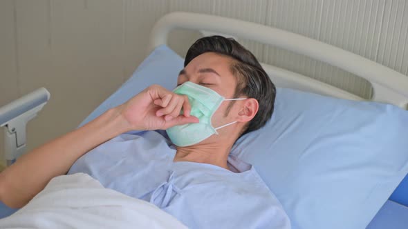 Unwell young Asian male patient coughing while rest lying in hospital bed recovery after fell ill. alt