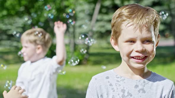 Little Boy Smiling at Camera at Bubble Show in Park alt