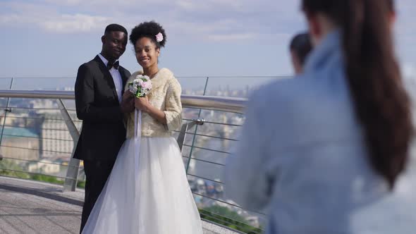 Happy African American Newlyweds Posing for Photographer on Bridge on Sunny Summer Day alt