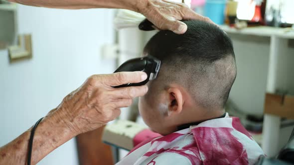 The barber is cutting hair and designing hairstyles for asian little boy. alt