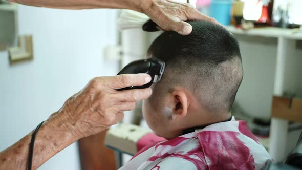 The barber is cutting hair and designing hairstyles for asian little boy.