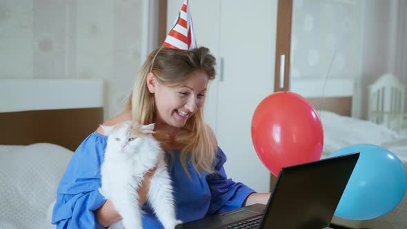 Social Distancing, Young Woman with Domestic Cat with Festive Balloons and Pipe Congratulates Her alt