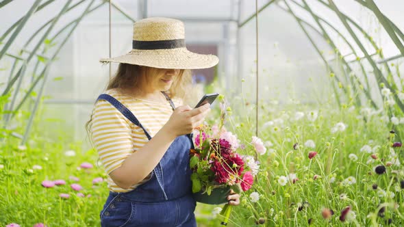 Woman with Fresh Flowers Uses Mobile Phone in Greenhouse