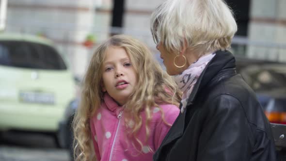 Portrait of Cute Girl Talking with Granny Sitting on Bench on City Street Outdoors alt