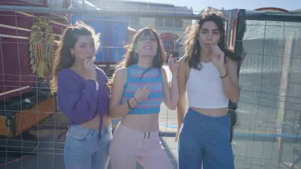 Three Darkhaired Girls with Lollipops By Metal Fence on Windy Day alt