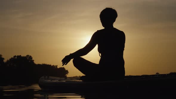 Silhouette of Woman Practicing Yoga on SUP Board at Sunset alt