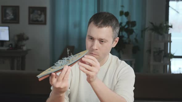 Adult cheerful man enthusiastically collects a plastic model of a historic ship.