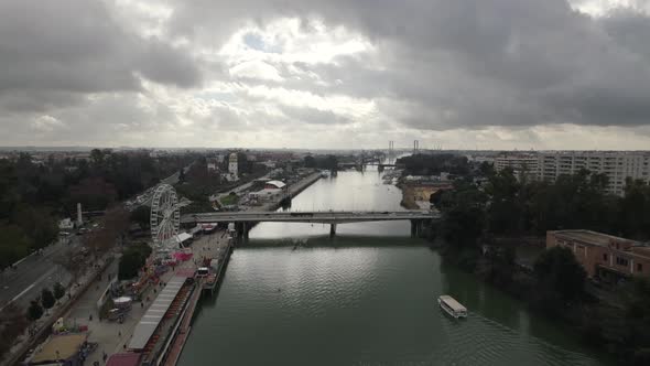 Drone flying over Guadalquivir river with amusement park and ferris wheel on shore, Seville in Spain