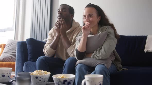 Excited Young Couple Relaxing At Home Sitting On Sofa Whilst Watching Sport On TV Together