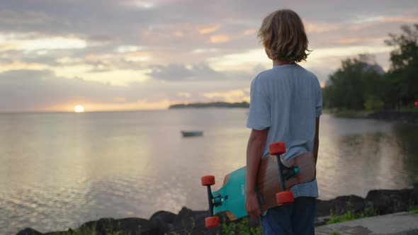 Silhouette Happy Child Portrait of Young Stylish Skater Boy Holding His Skateboard Outdoors alt