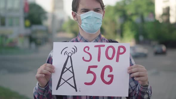 Camera Approaches To Stop 5G Placard in Hands of Caucasian Man in Face Mask. Male Activist alt