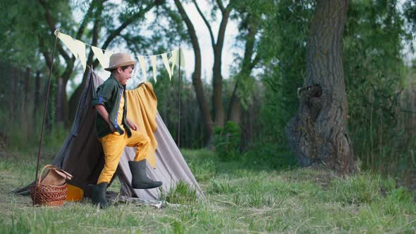 Kid Outdoor Active Boy in Hat and Rubber Boots Has Fun Throwing Stones Into Water on Vacation in alt