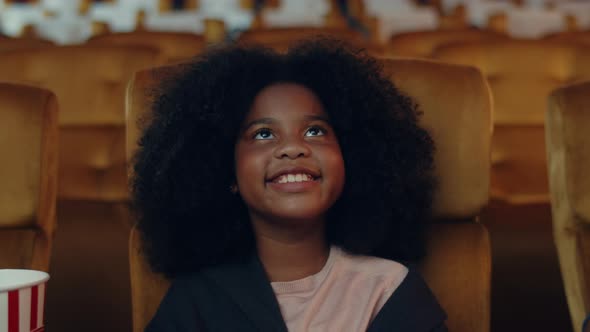 Attractive cheerful young black african girl laughing while watching film in movie theater.
