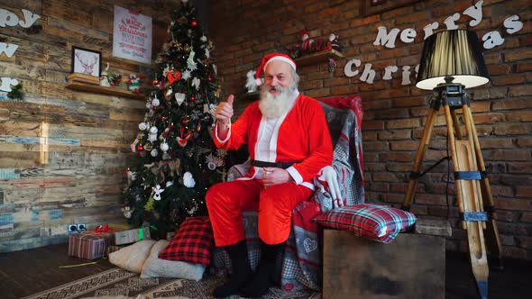 Energetic Santa Claus Raises Thumb Up, Sitting on Armchair in Festively Decorated Room
