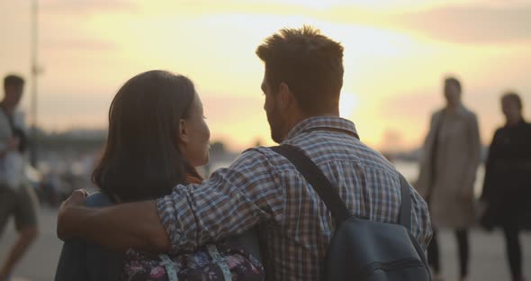 Back View of Young Couple Cuddling Enjoying Beautiful Sunset Together alt
