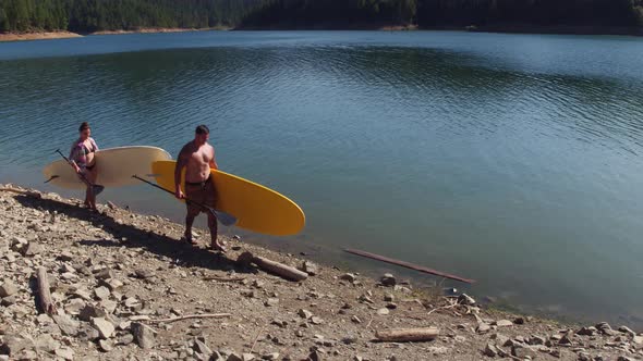 Couple walking by lake with stand up paddle boards alt