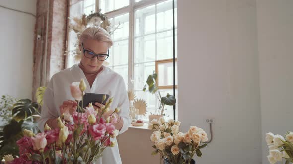 Professional Female Florist Examining Flowers and Using Digital Tablet alt