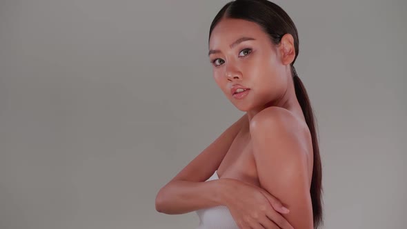 Beautiful girl applying moisturizer oil onto her body.  Asian young woman with tanned skin. alt