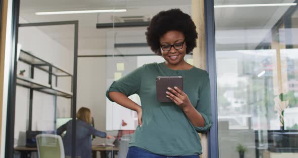 African american businesswoman leaning in doorway using tablet smiling to camera in office alt