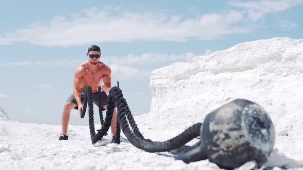 A strong muscular athlete makes strength exercises for the body with a rope. alt