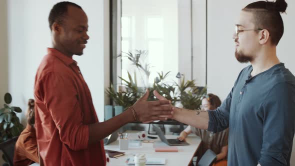 Multiethnic Male Colleagues Greeting Each Other and Talking in Office alt