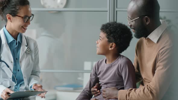 Little African American Boy Speaking and Giving High Five to Female Pediatrician alt
