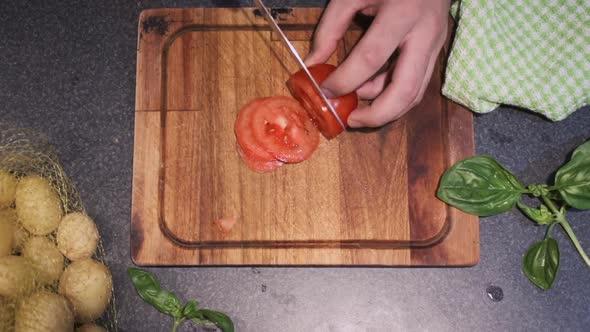 Young male slicing a tomato in his kitchen on top of a cutting board with a sharp knife alt