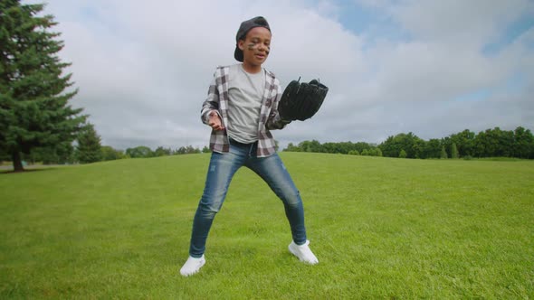 Joyful School Age African Boy with Baseball Glove and Ball Dancing on Field alt