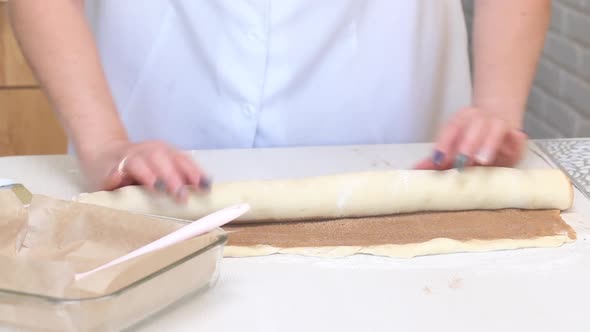 The Woman Rolls The Cinnabon Dough, Sprinkled With Cinnamon. On A White Tabletop. Close Up Shot alt