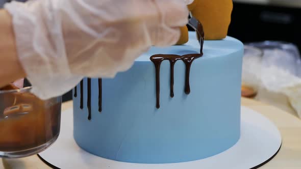 Pastry Chef in Gloves Pour Liquid Chocolate on a Blue Cake with a Spoon