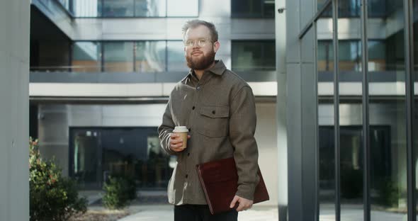 A Bearded Man Standing in the Courtyard of Office Center and Looking at Camera alt