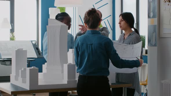 Group of Diverse People Working on Design of Building Model with Laptop and Blueprints alt