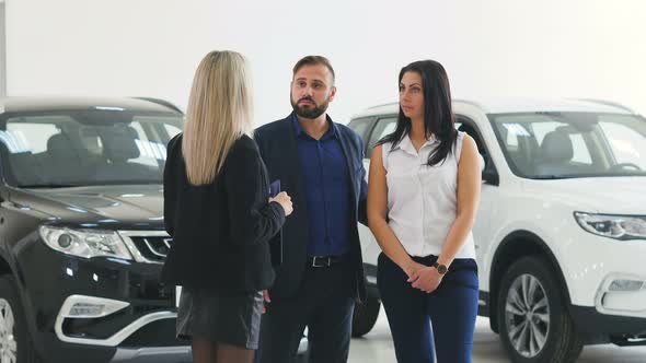 Cavcasian Saleswoman with Clipboard Talking with Couple Choosing Car at Dealership