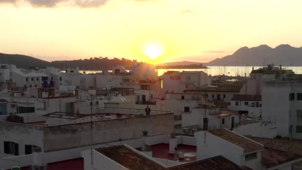 AERIAL: Guy Standing on Roof of Small Townhouse with Port on Tropical Island with Boats and Ocean at alt